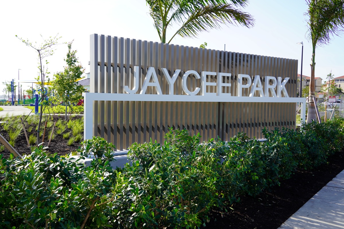 Modern “Jaycee Park” entrance sign framed by lush landscaping and palm trees.